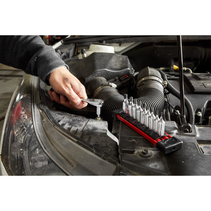 Person working on a car engine with a tool set beside them.
