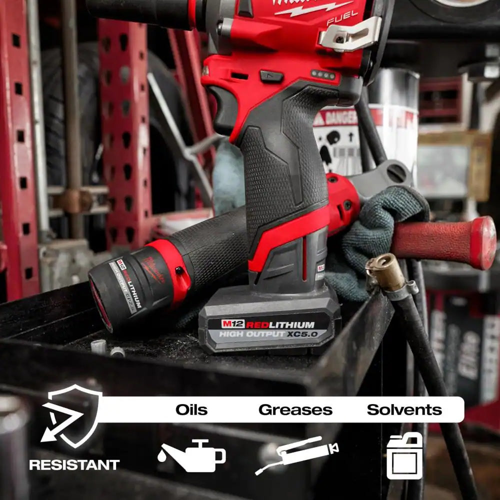 Red and black cordless drill on a workbench with text indicating oil, grease, and solvent resistance.