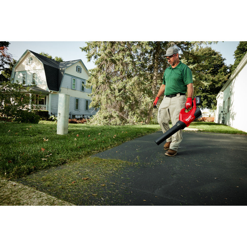 Man using an M18 FUEL™ Blower on a driveway in a suburban neighborhood.