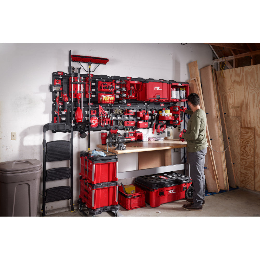 Person in garage organizing tools on a wall-mounted PACKOUT organizer.